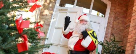 Der Weihnachstsmann steht vor einer geschmückten Tür und bringt Geschenke