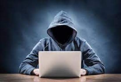eine anonyme Person sitzt bedrohlich vor einem Rechner.