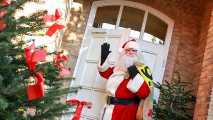 Der Weihnachstsmann steht vor einer geschmückten Tür und bringt Geschenke